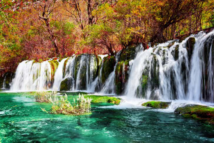 Beautiful waterfall and azure lake with crystal clear water among fall woods in Jiuzhaigou nature reserve