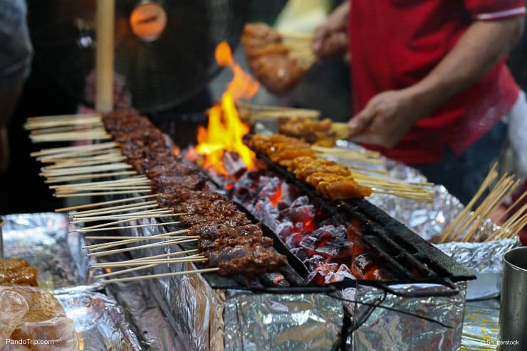Skewers of chicken cook over hot coals in Singapore's Satay Street food market