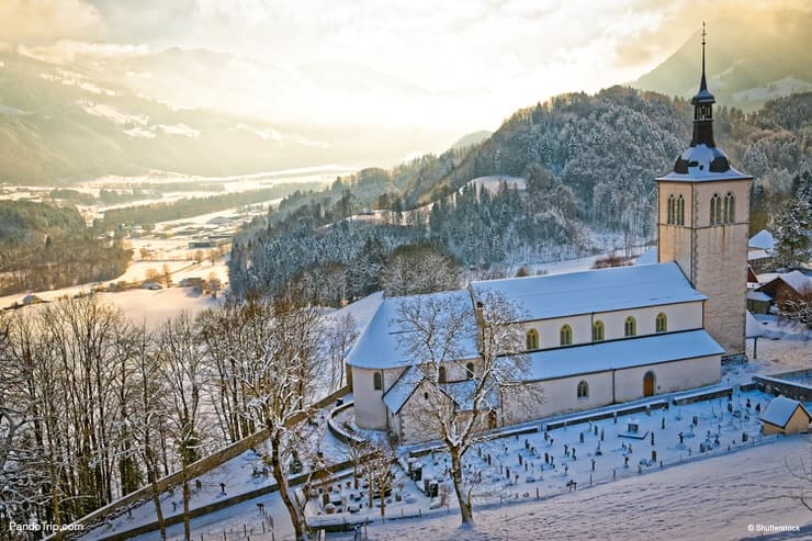 Picturesque snow-covered mountain landscape near the castle of the Gruyeres with an old church in the foreground. Winter in Switzerland