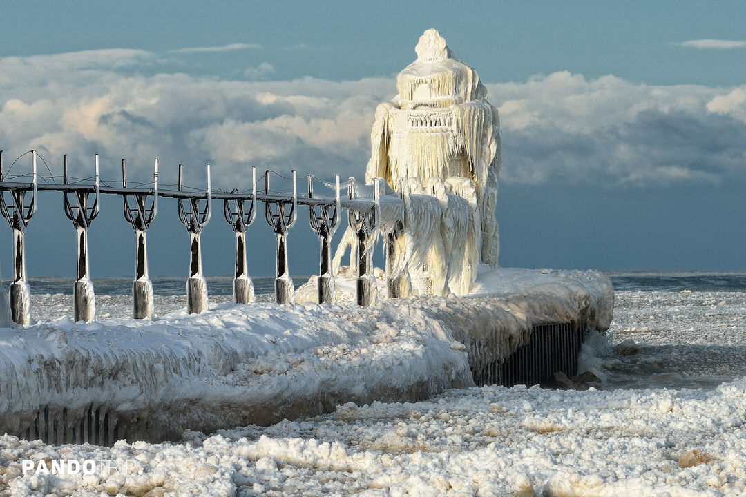 Ice-covered St. Joseph North Pier Lighthouse and catwalk on frozen Lake Michigan after a winter storm, coated in thick icicles