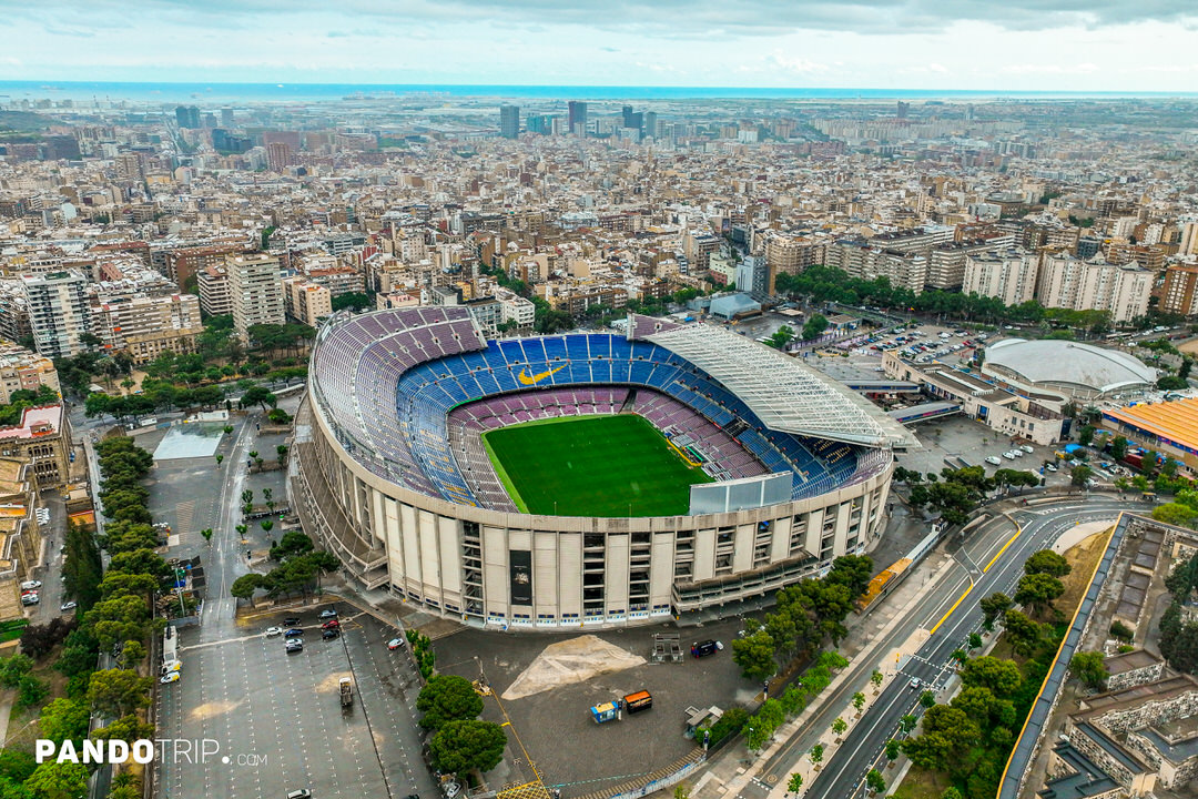 Aerial view of Camp Nou stadium in Barcelona with cityscape and coastline in the background.