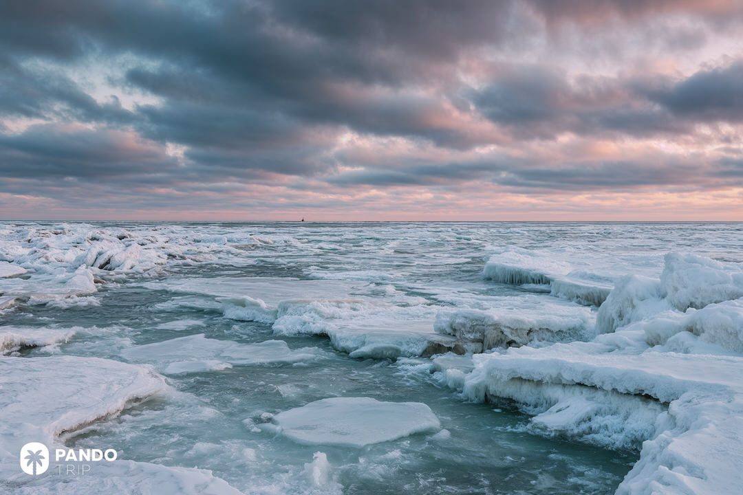 Expansive frozen landscape on the edge of Lake Michigan, covered in thick ice slabs under dramatic evening clouds.