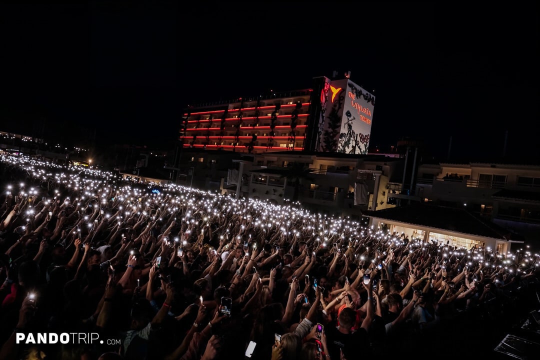 Festival crowd holding up lit smartphones in front of the illuminated Ushuaïa Tower nightclub at night.