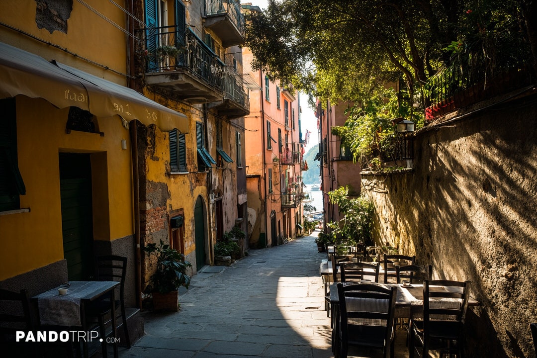 A peaceful alley in Vernazza with outdoor tables and colorful buildings in warm light.