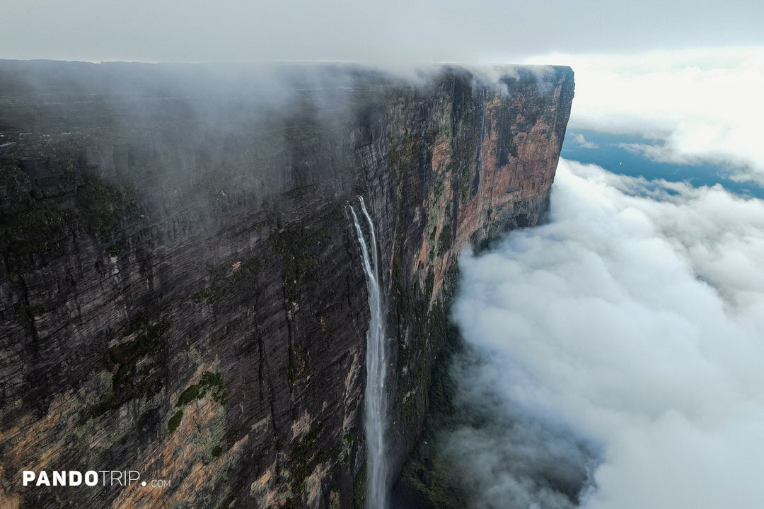 Aerial view of waterfalls flowing from Mount Roraima’s cliff face into dense clouds below