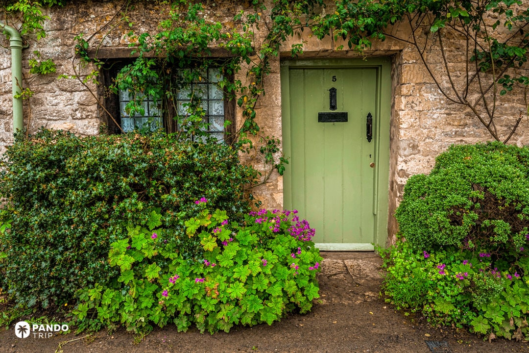 Pale-green cottage door framed by flowers on Arlington Row Bibury