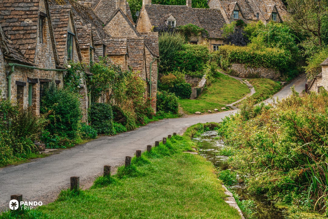 Path and stream running beside Arlington Row cottages in Bibury on a lush summer day