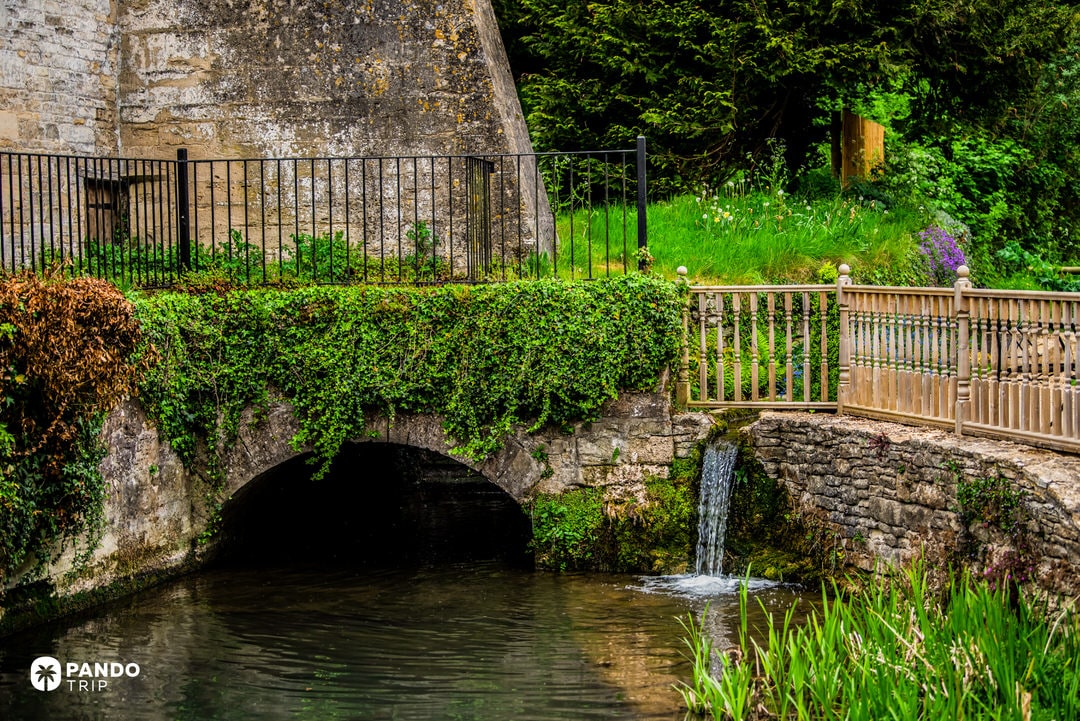 Small ivy-covered stone bridge and waterfall on a tributary of the River Coln in Bibury
