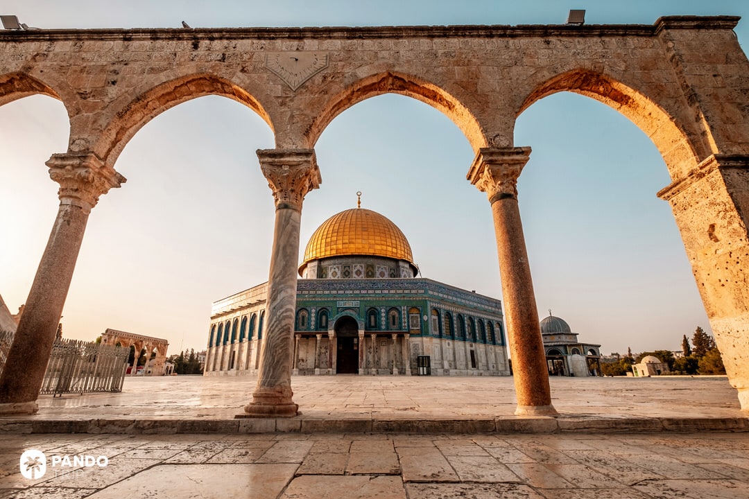 The golden Dome of the Rock mosque framed by old stone arches at dawn in Jerusalem
