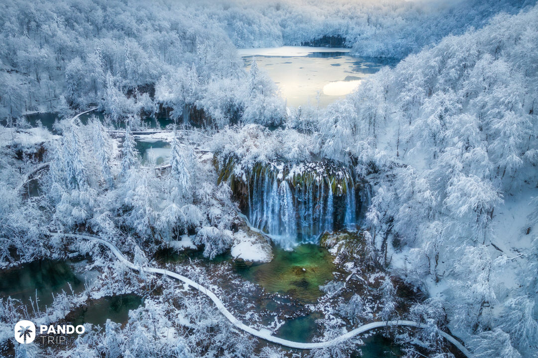 Aerial photo of Plitvice Lakes National Park in winter with snow-covered forest, frozen waterfalls, and turquoise pools