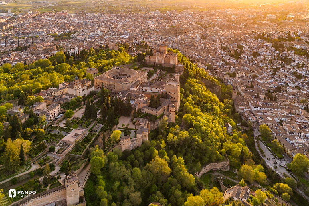 Aerial sunset view of the Alhambra Palace above Granada and lush Generalife gardens.