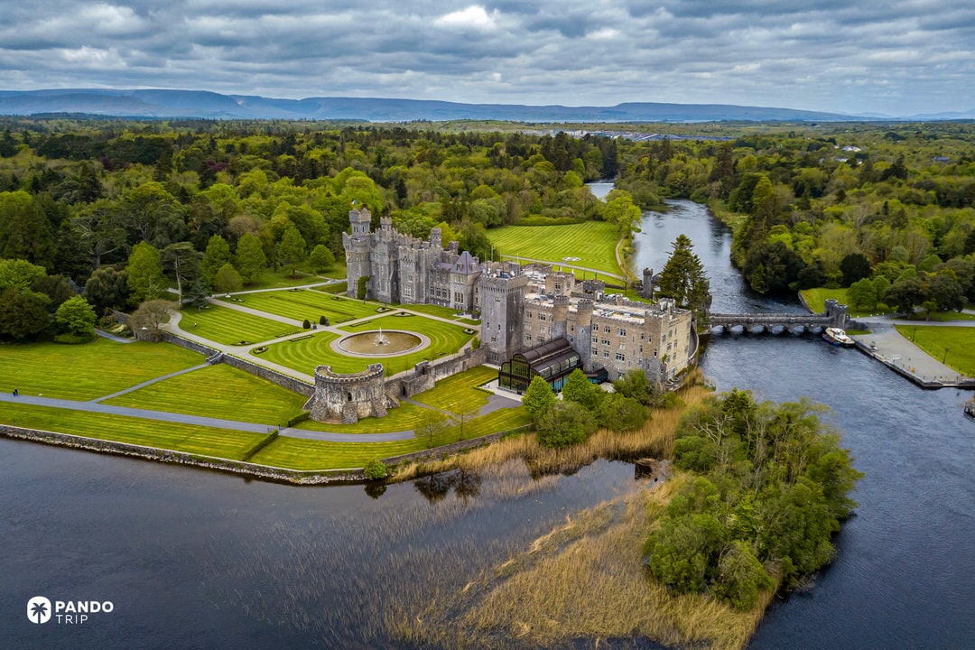 Drone photo of Ashford Castle on Lough Corrib, framed by lawns, forest and river.