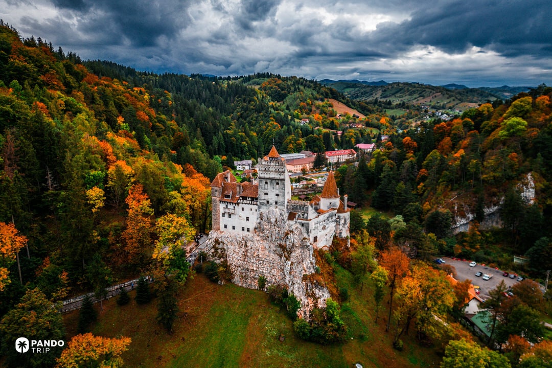 Bran Castle nestled among autumn forests under dramatic storm clouds in Transylvania.