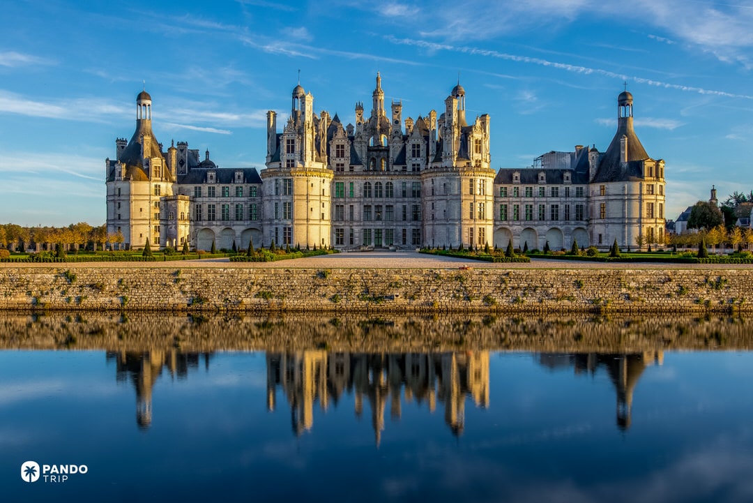 Château de Chambord reflected symmetrically in still water at sunrise.