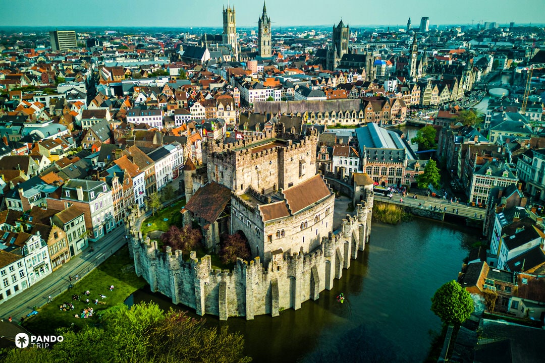 Drone shot of Gravensteen Castle encircled by moat amid Ghent’s city rooftops.
