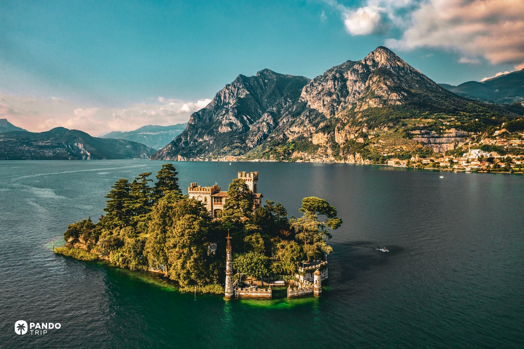 Tiny Isola di Loreto with neo-Gothic castle amid Lake Iseo, Alps in background.