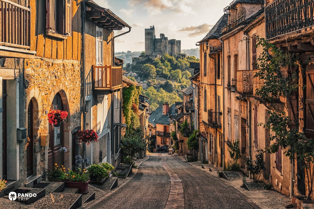 View up village street toward Najac Castle atop ridge at golden hour.