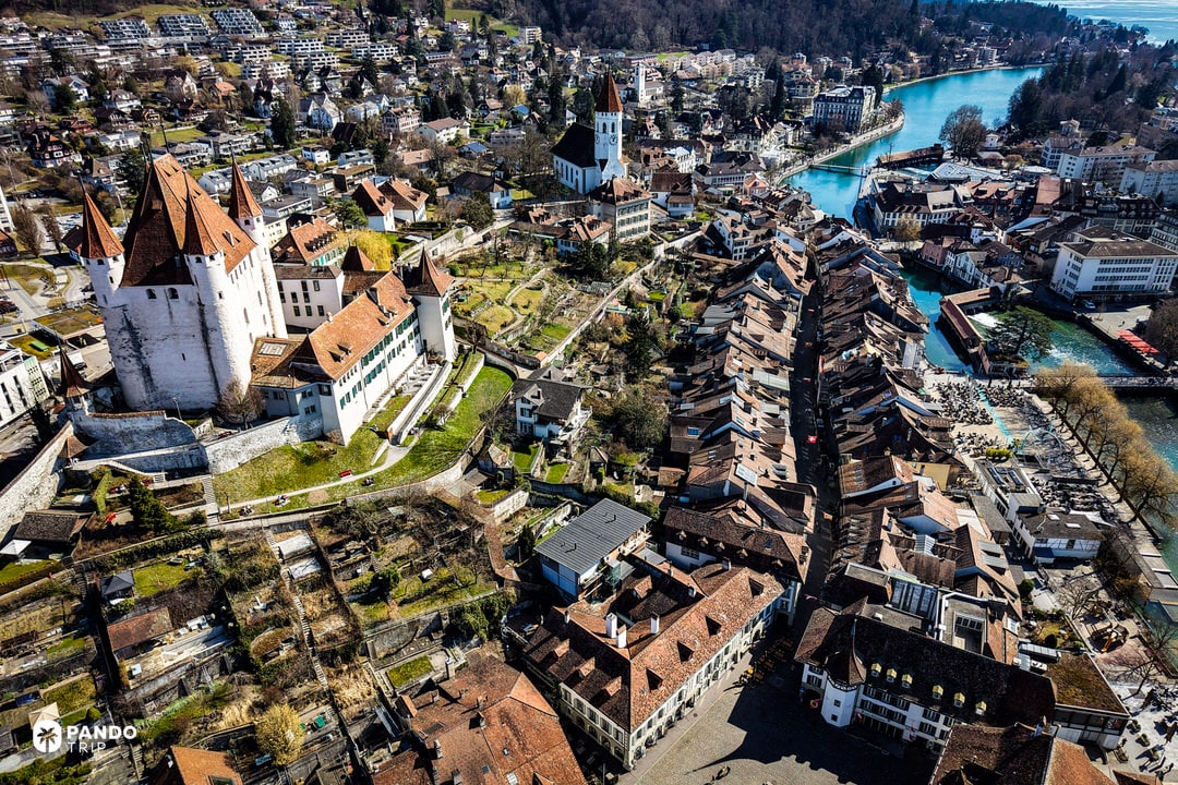 Bird’s-eye view of Thun Castle’s four towers above Swiss rooftops and the turquoise Aare River.