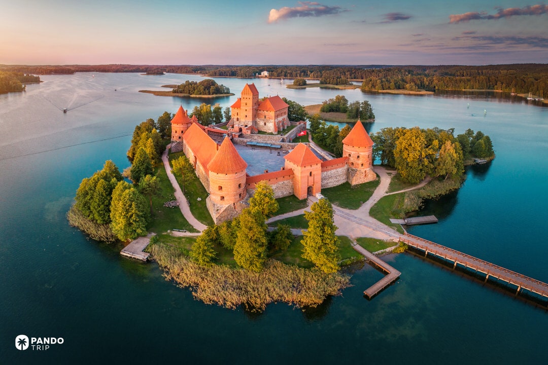 Island Trakai Castle with red-brick towers surrounded by blue Lake Galvė at sunset.