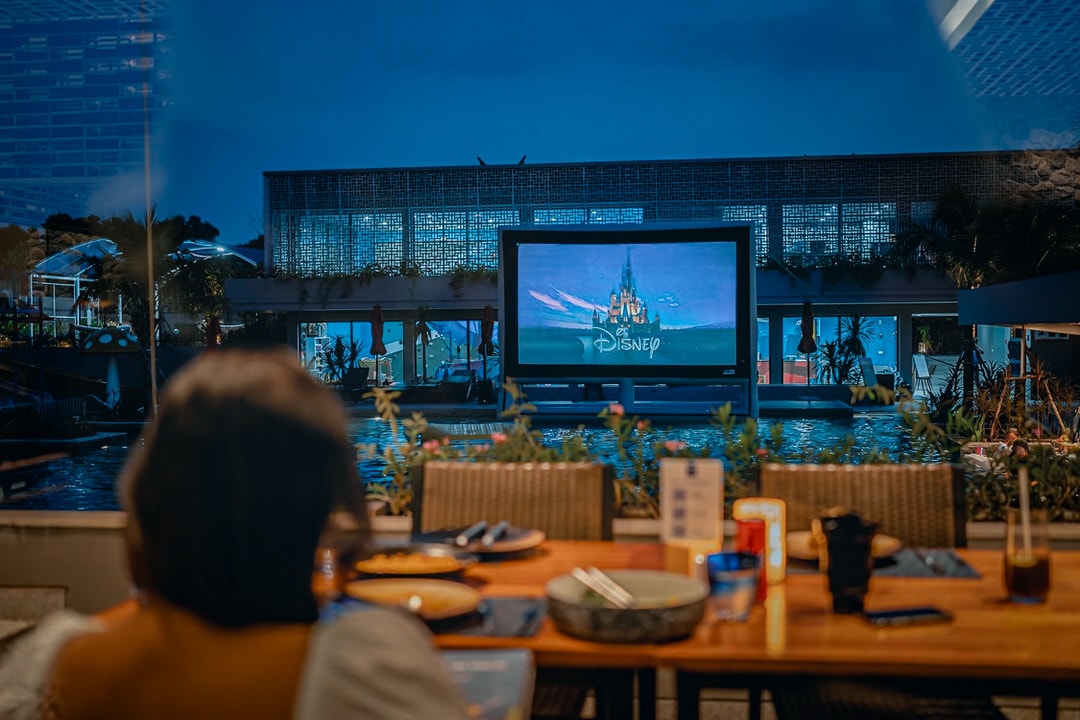 Guest dining while watching a Disney film on a floating screen at Anantara Mai Khao Phuket’s poolside dive-in cinema in Thailand