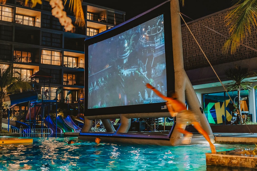 Children swimming and jumping into the pool during Anantara Mai Khao Phuket’s dive-in movie night with a large inflatable screen