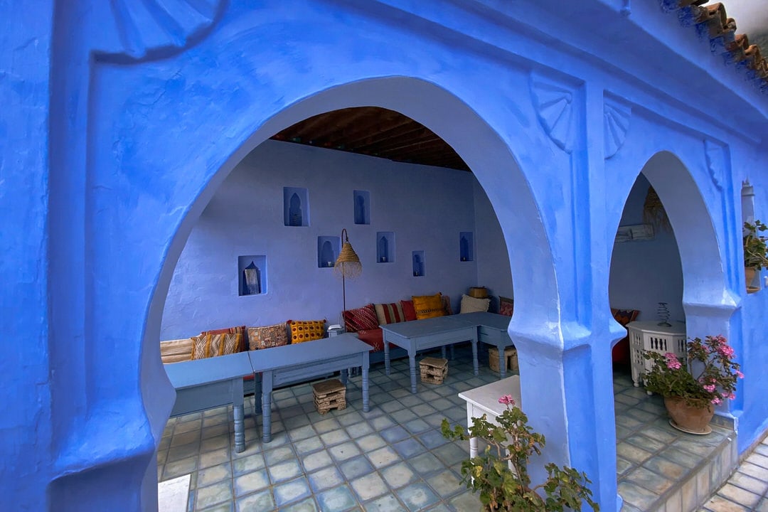 Traditional riad courtyard at Casa Perleta in Chefchaouen with blue arches, seating, and Moroccan decor