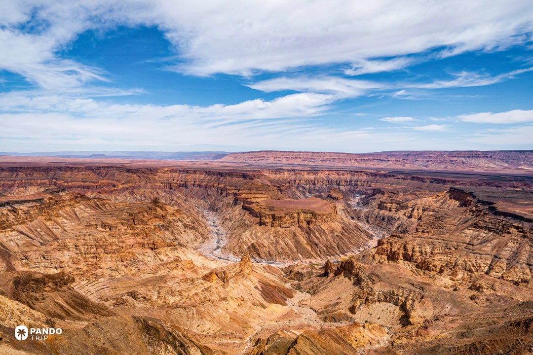 Wide panorama of Namibia’s Fish River Canyon, desert terraces and buttes with the river winding far below beneath high clouds.