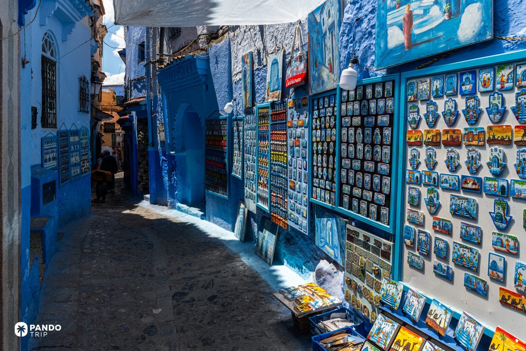 Blue-painted alley in Chefchaouen with walls covered in souvenirs, magnets, and traditional crafts