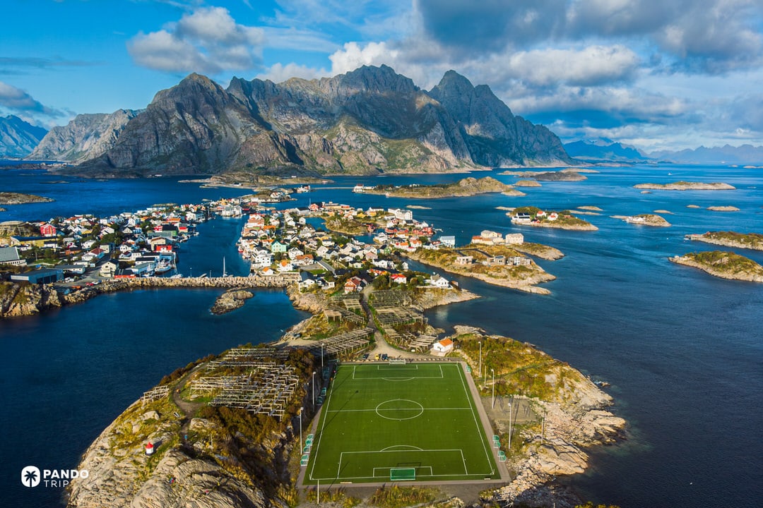 Aerial of Henningsvær Stadium on a rocky islet surrounded by turquoise water in the Lofoten Islands.