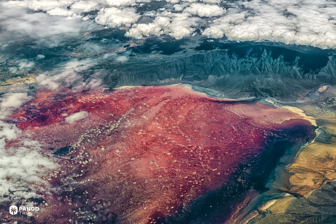 Aerial of Lake Natron with nearby volcanic cone and reddish shallows.