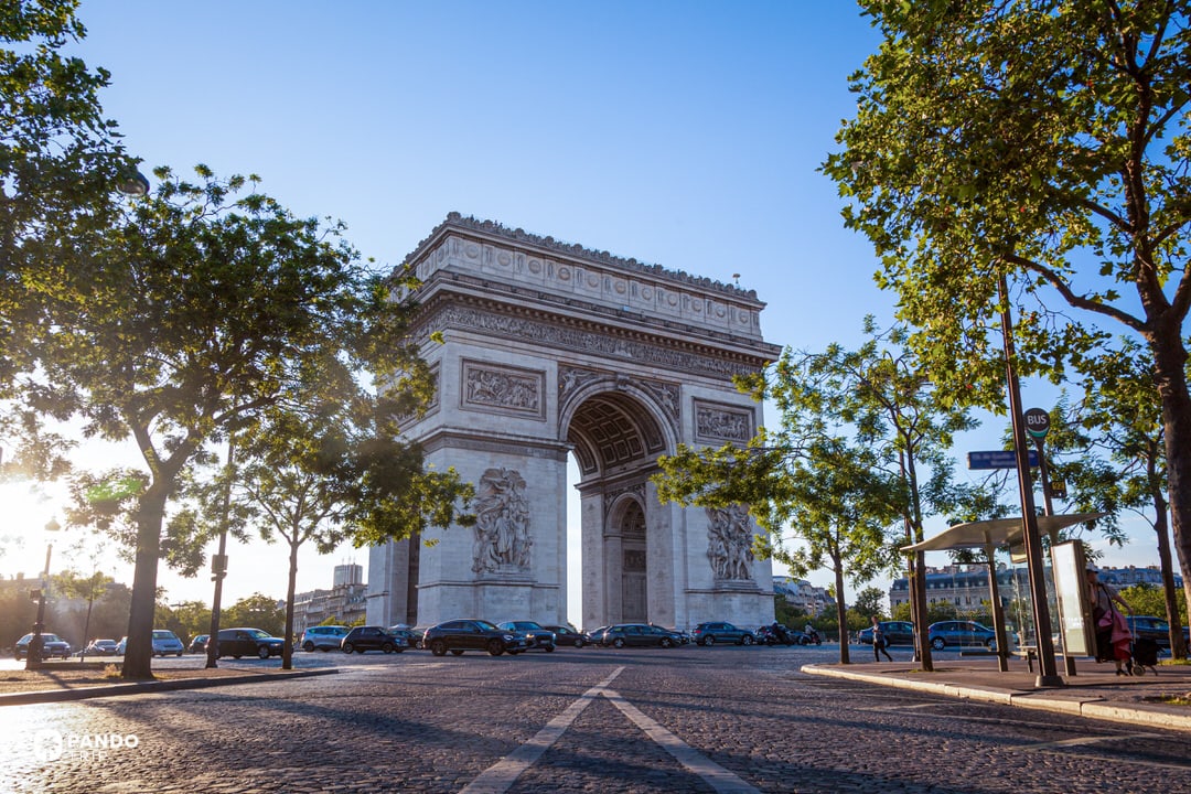 Street-level view of the Arc de Triomphe at Place Charles-de-Gaulle in Paris, framed by trees.