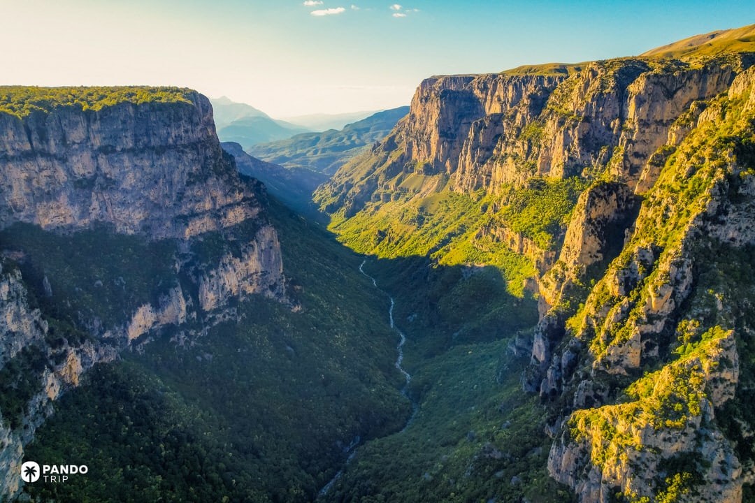 Vikos Gorge in Greece’s Pindus Mountains, towering limestone cliffs and a thin river far below, bathed in soft afternoon haze.